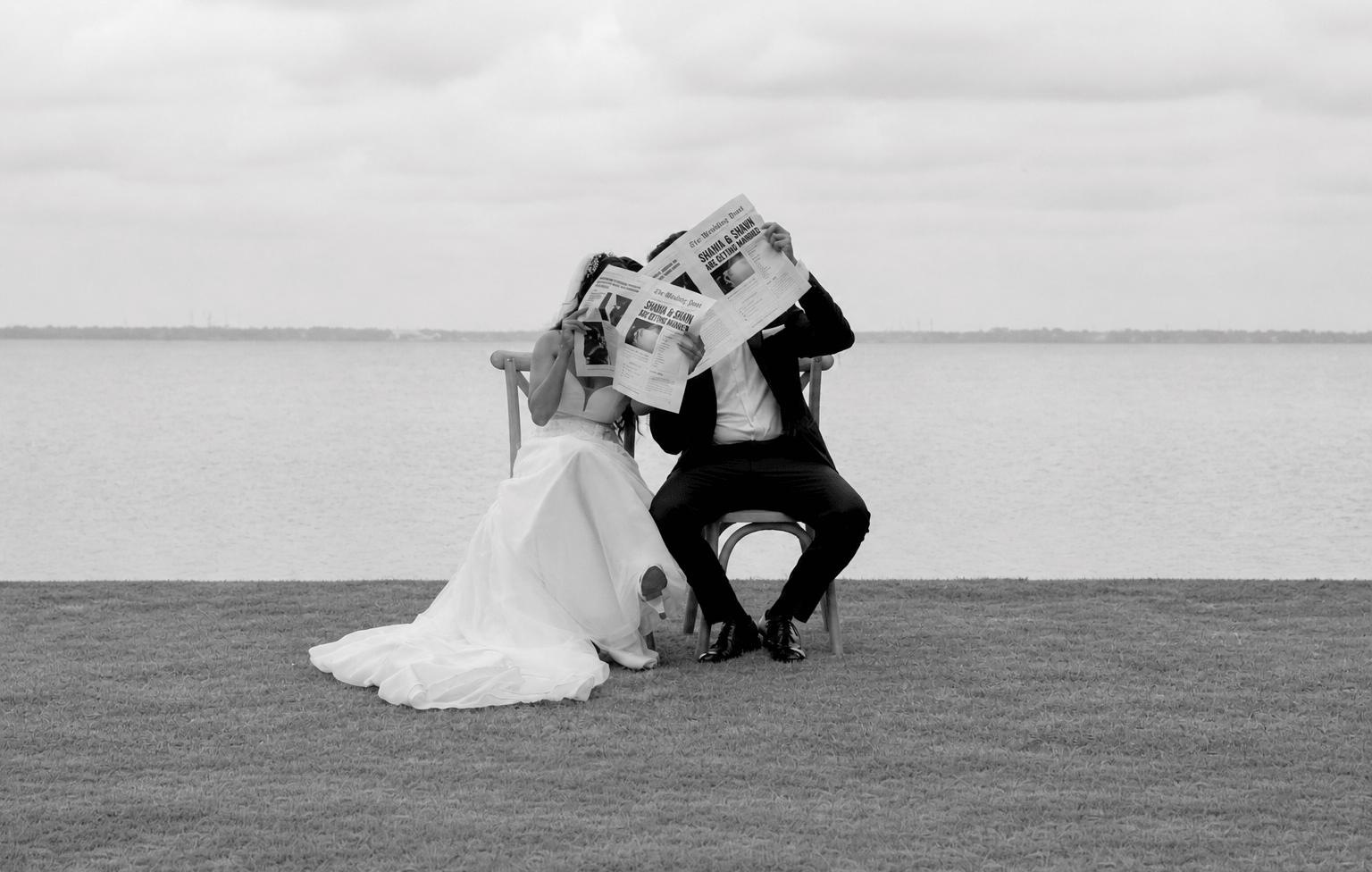 Wedding couple reading a newspaper by the water
